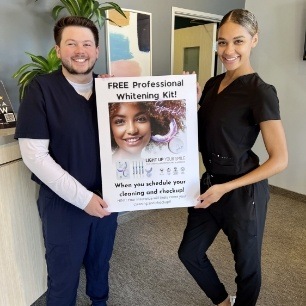 Two dental team members holding a free teeth whitening deal poster