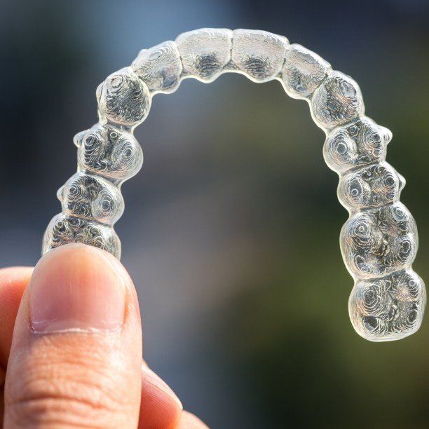 Hand holding an Invisalign clear braces tray