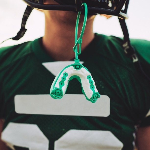 Football player with athletic mouthguard hanging from helmet