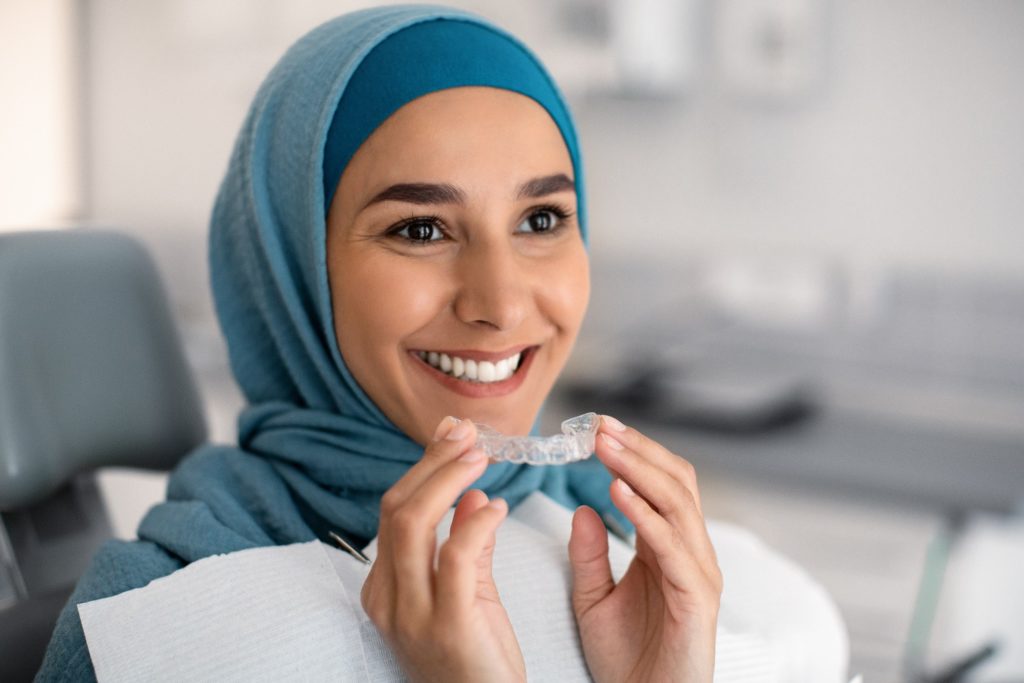 Woman smiling while holding Invisalign aligner